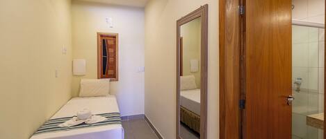 A hotel room with a bed, a mirror, a wooden door, and a shower area.