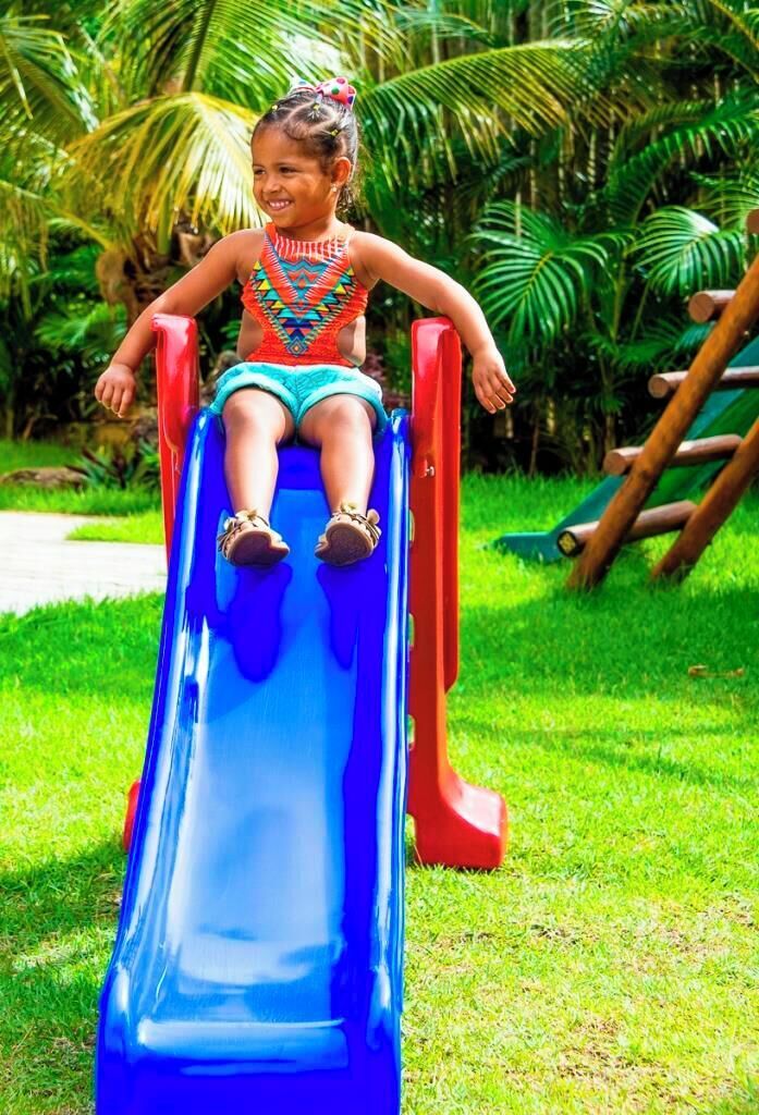 A child on a blue slide in a grassy area with a wooden structure in the background.
