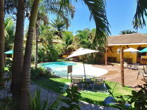 A pool area with lounge chairs and umbrellas, surrounded by palm trees and a yellow building.