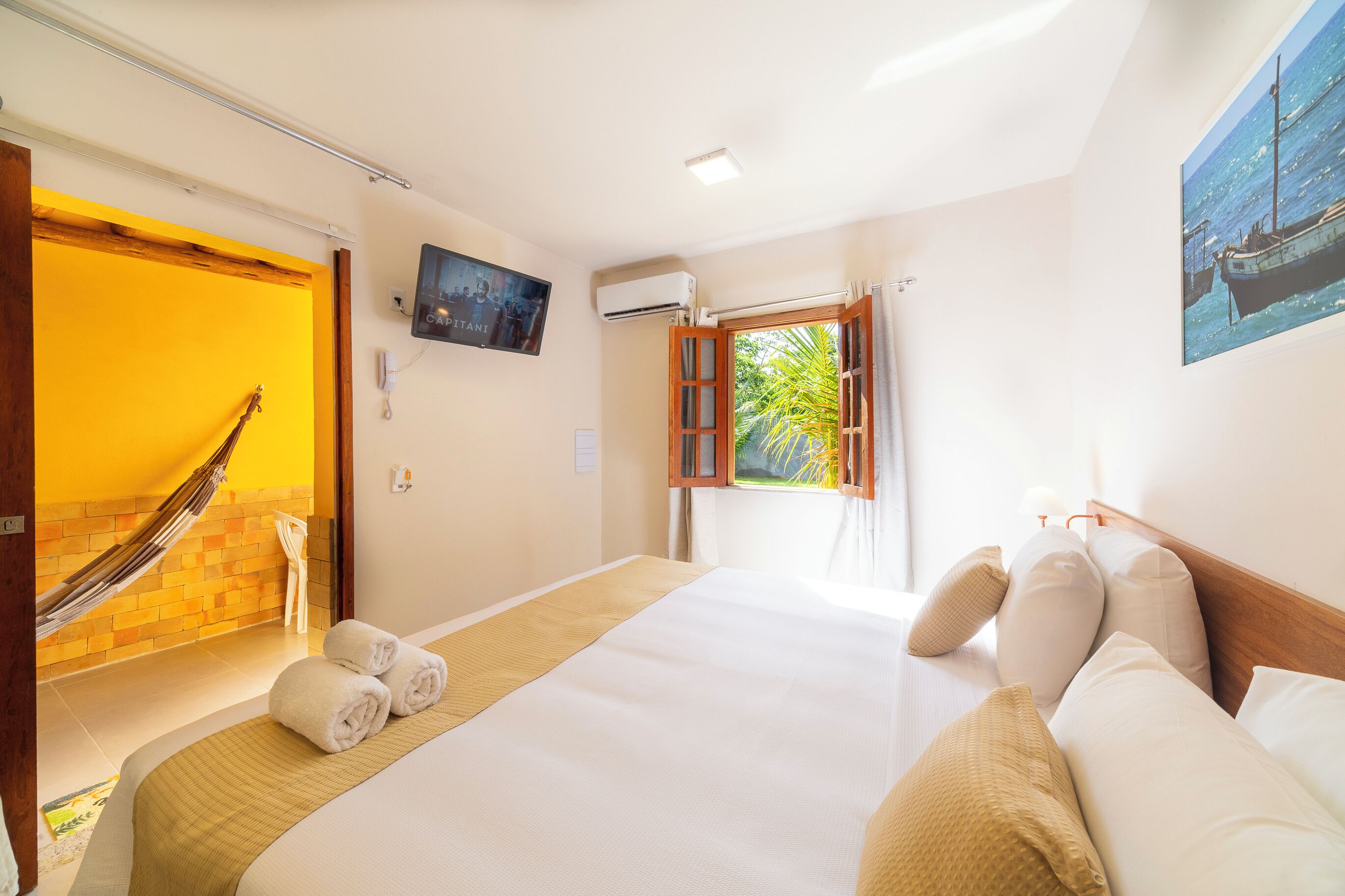 A hotel room with a bed, a hammock, a TV, an air conditioning unit, and a window with curtains.