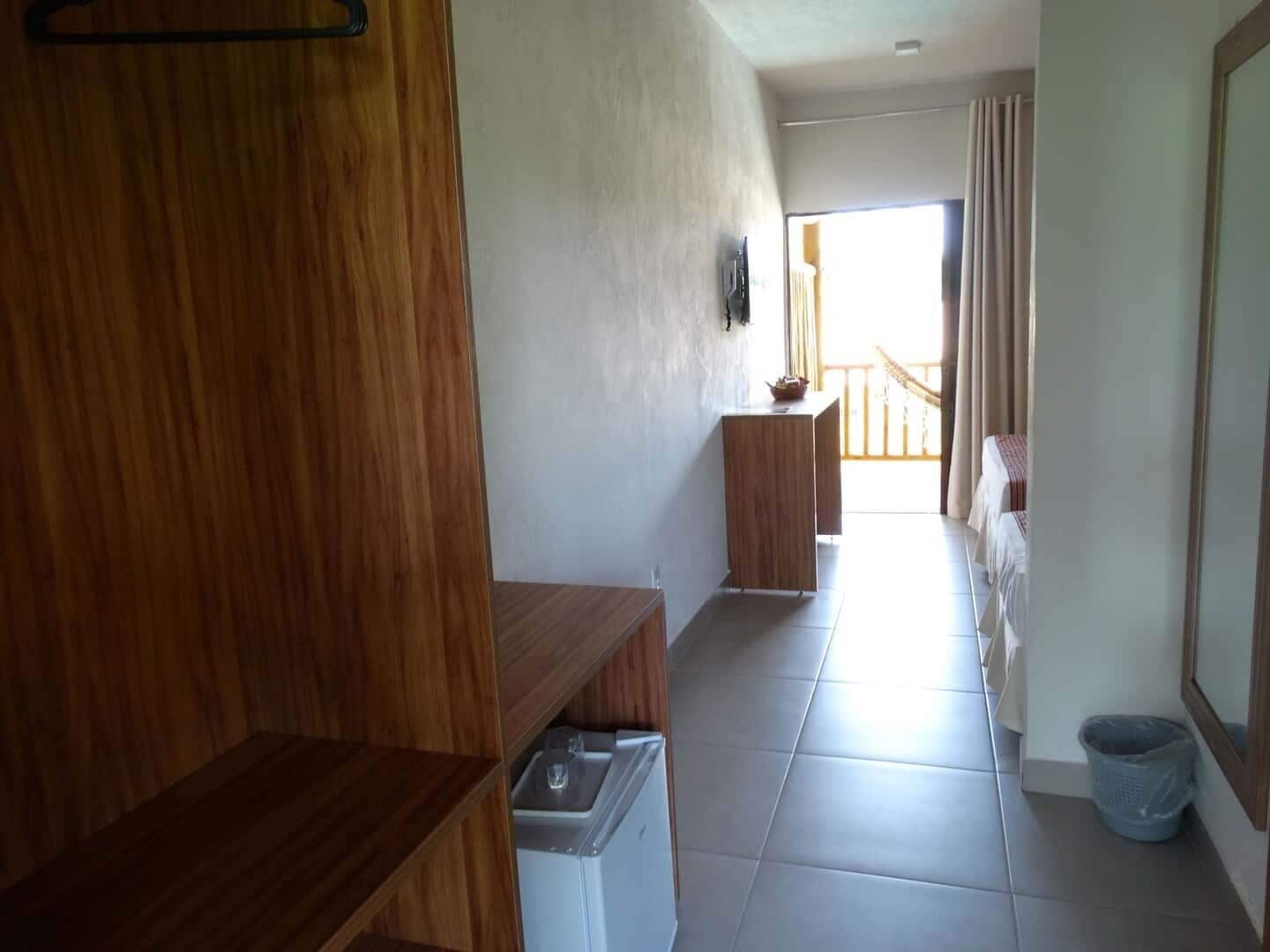 Ein Hotelzimmer mit Holzschrank, einem kleinen Schreibtisch, einer Waschmaschine, einem Bett mit gestreifter Bettdecke und einem Balkon mit Aussicht.