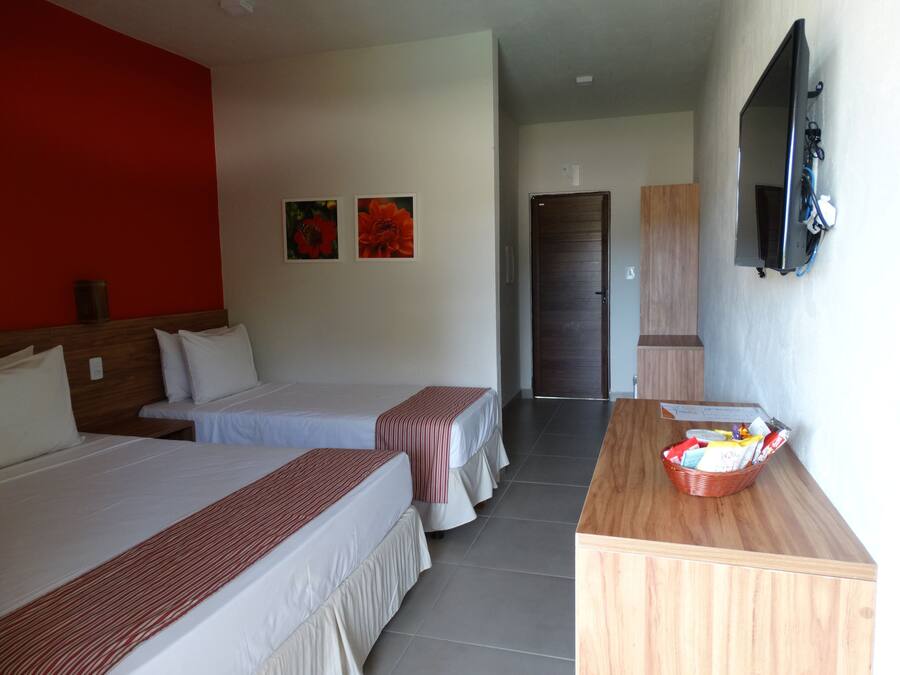 Ein Hotelzimmer mit zwei Betten, einem Holztisch, einem Fernseher und einer Tür zu einem weiteren Raum.