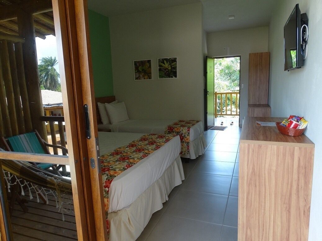A room with two beds, a wooden desk, a television, and a balcony with a view.