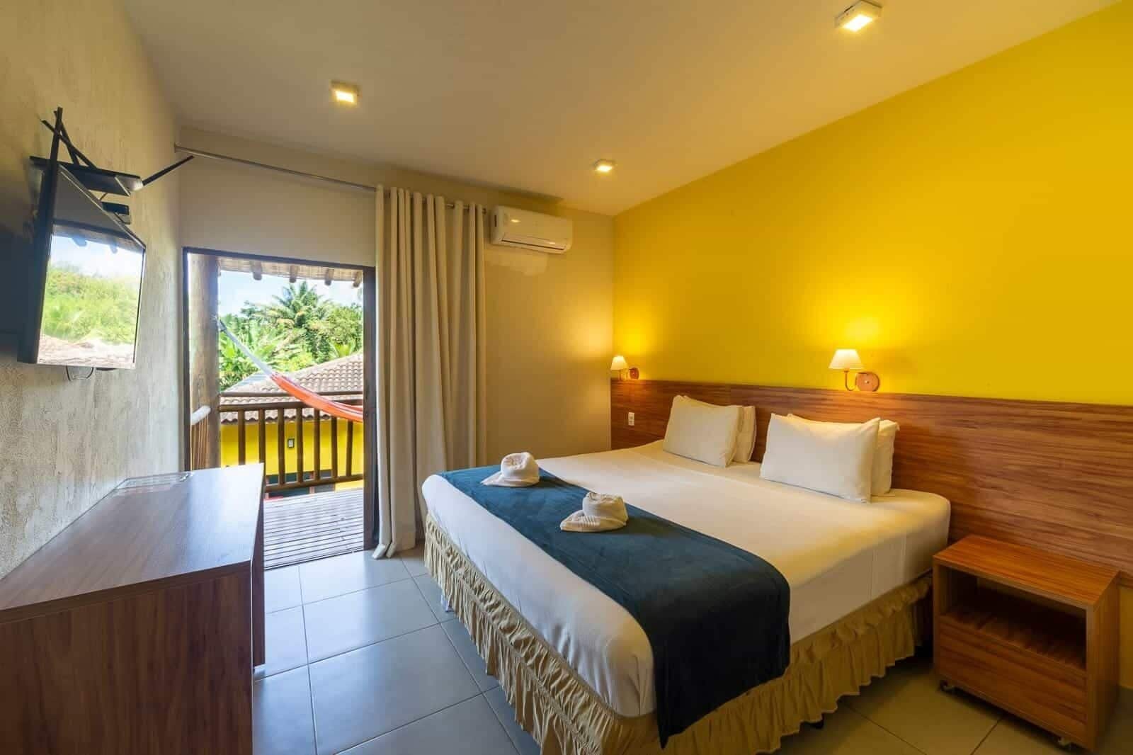 A hotel room with a bed, bedside tables, a desk, and a balcony with curtains.