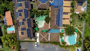 Vista aérea de un complejo turístico con varias piscinas, paneles solares y palmeras.