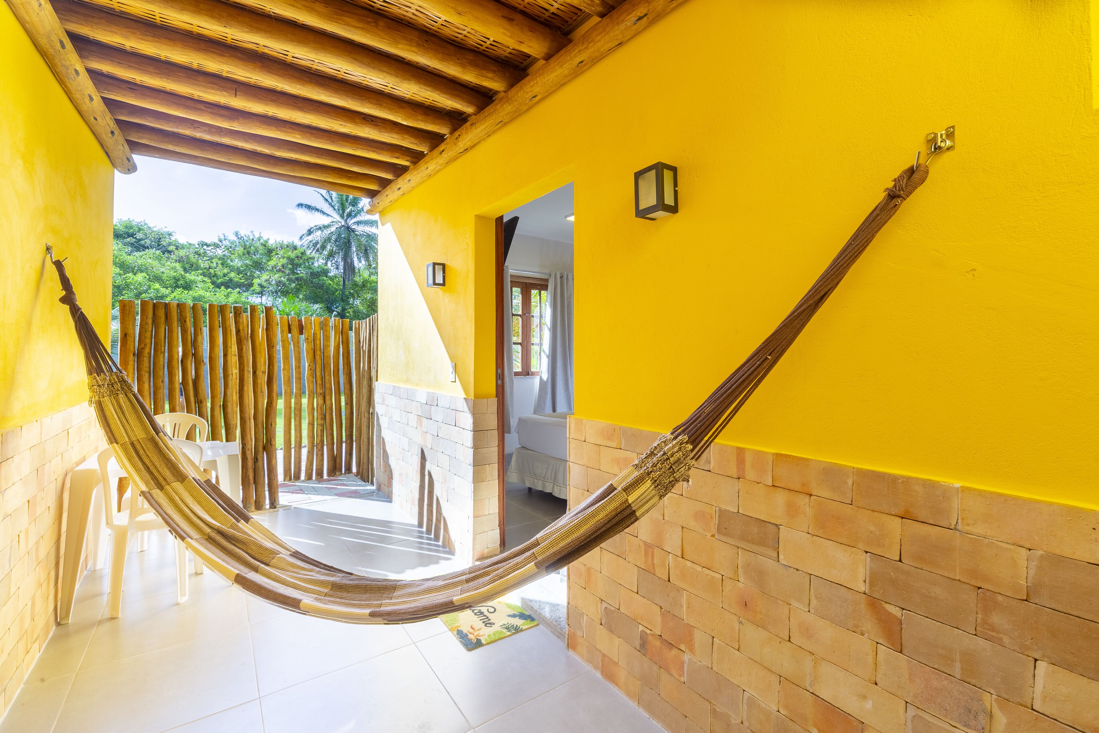 A hammock in a bright yellow corridor with a wooden ceiling and tiled floor.