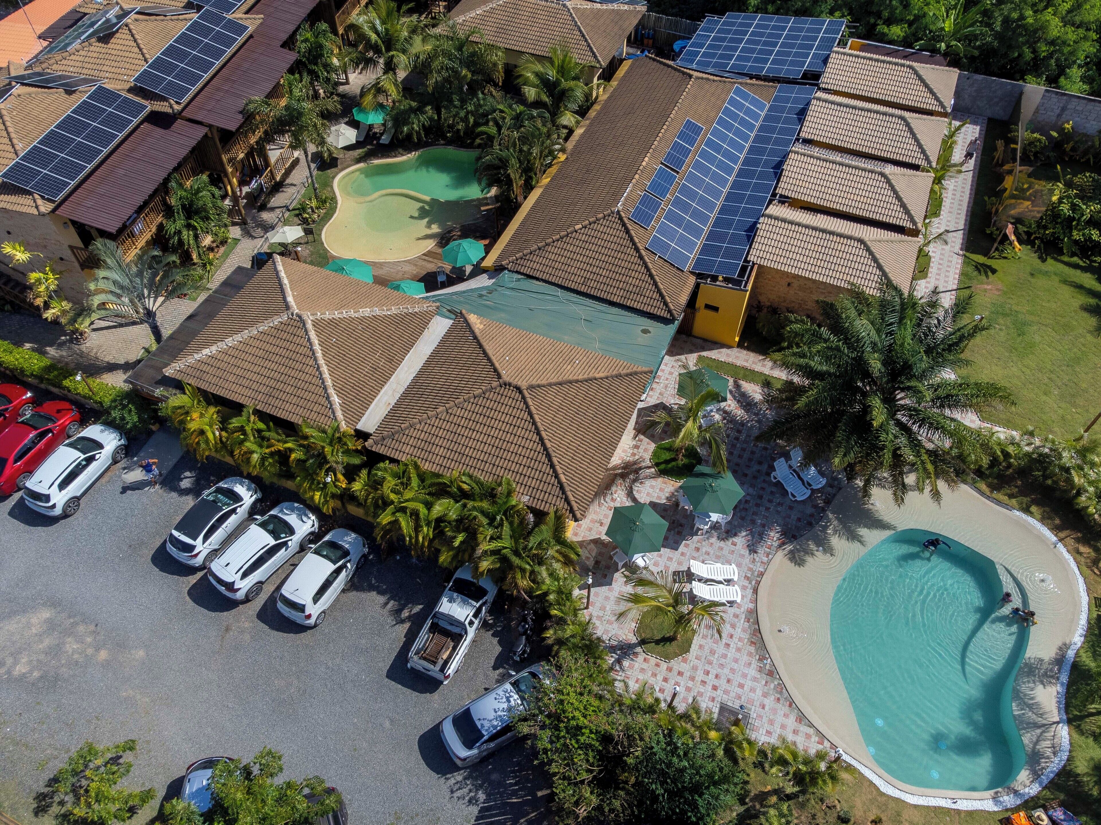 Vista aérea de un complejo turístico con varias edificaciones, una piscina y paneles solares.