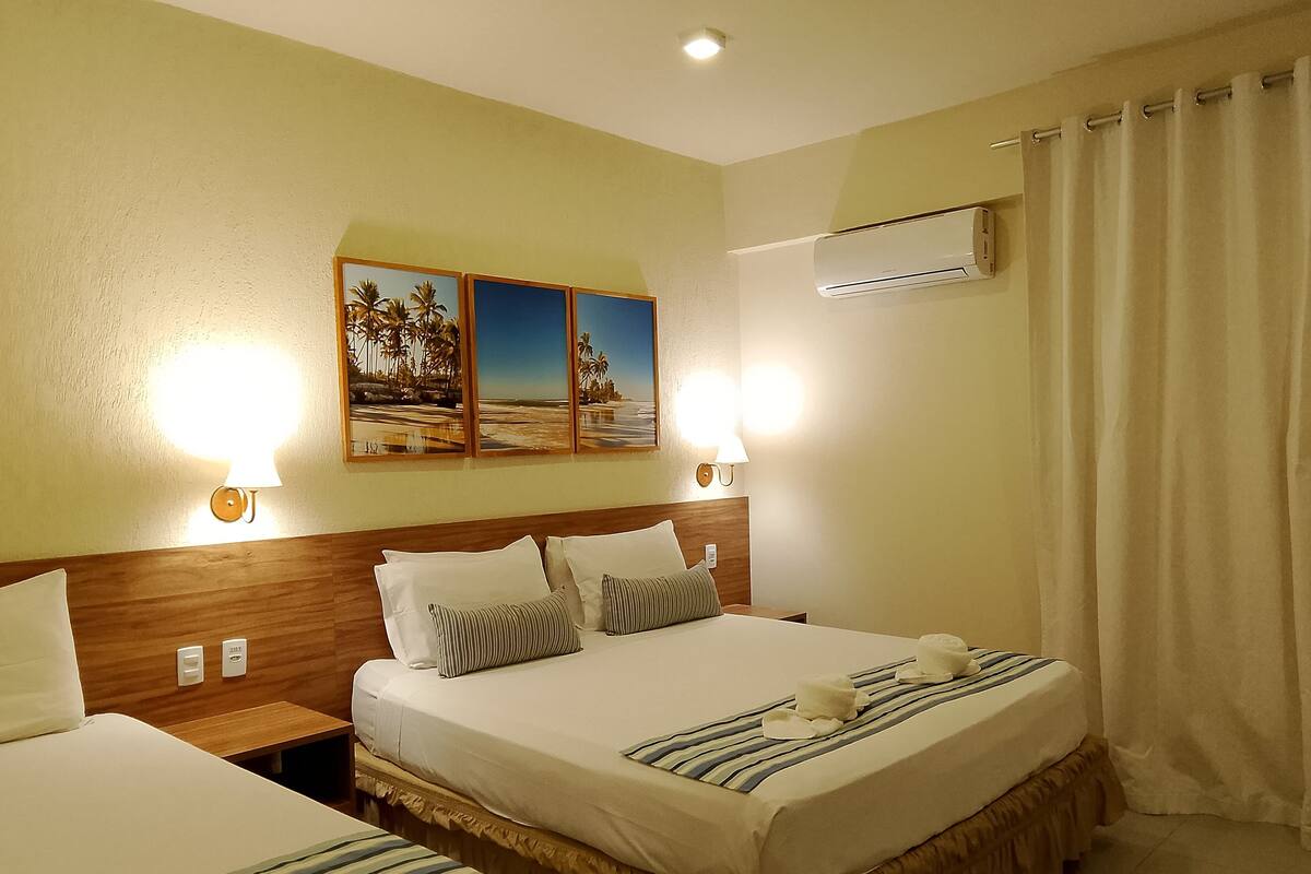 Ein Hotelzimmer mit einem großen Bett, zwei Nachttischen, einer Wandlampe und einem Strandbild über dem Bett.