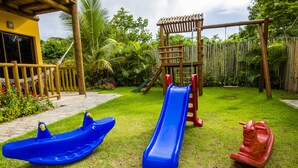 Un área de juegos infantiles con un tobogán, un pequeño bote y un caballo balancín.