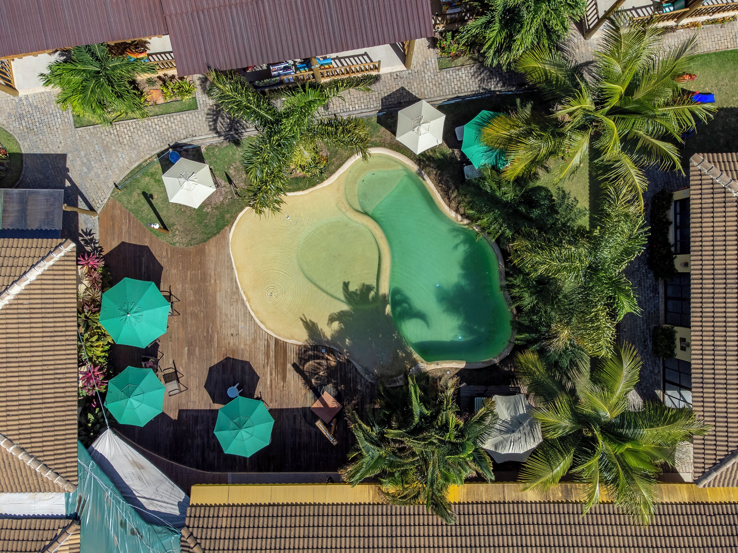Vista aérea de um resort com piscina, palmeiras e áreas de estar ao ar livre.