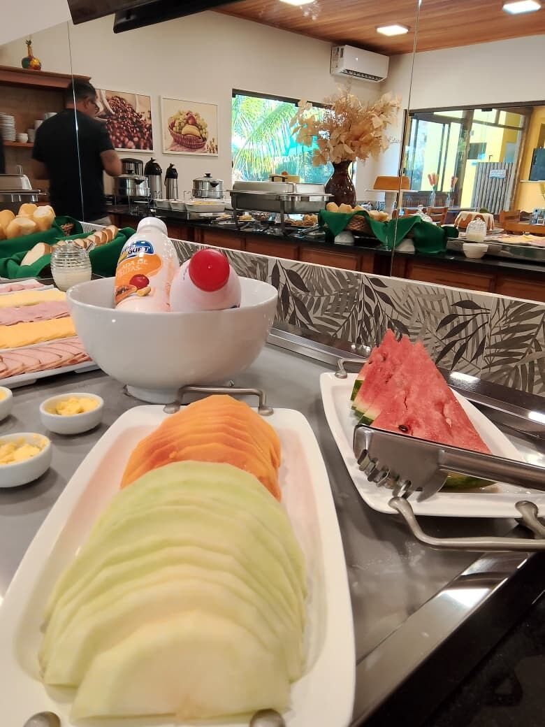 Een buffet met diverse gerechten, waaronder gesneden fruit, een soepkom en een stuk watermeloen.