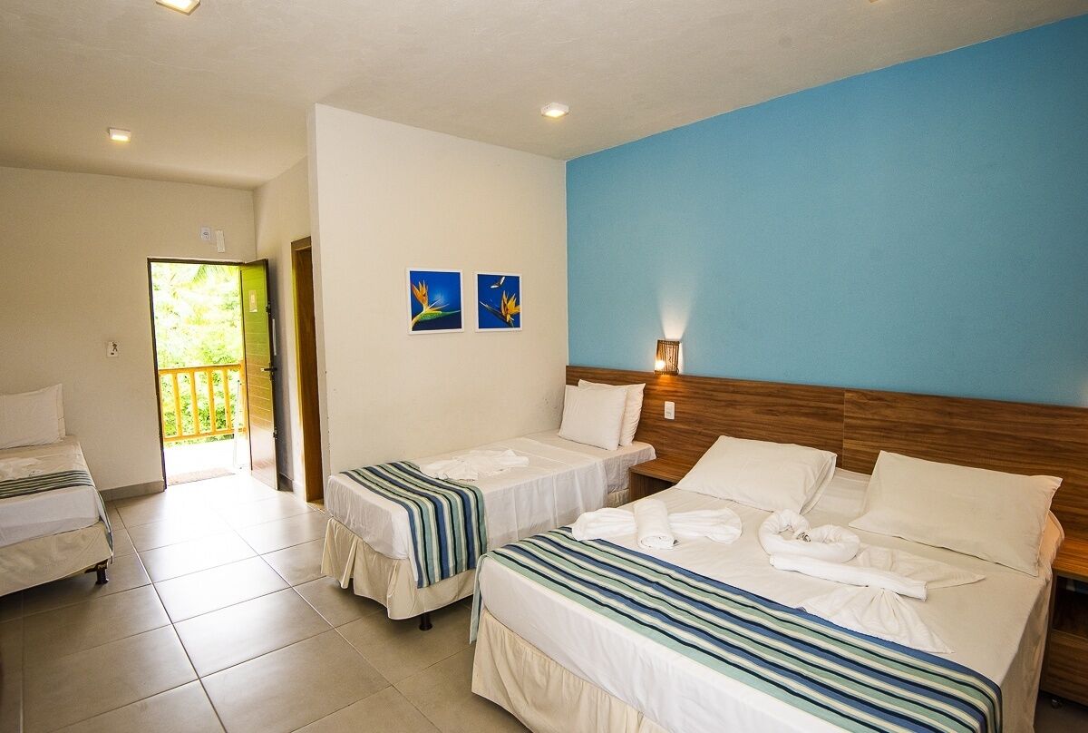 Une chambre d’hôtel avec deux lits simples, une tête de lit en bois, une porte-fenêtre donnant sur un balcon et deux tableaux accrochés au mur.