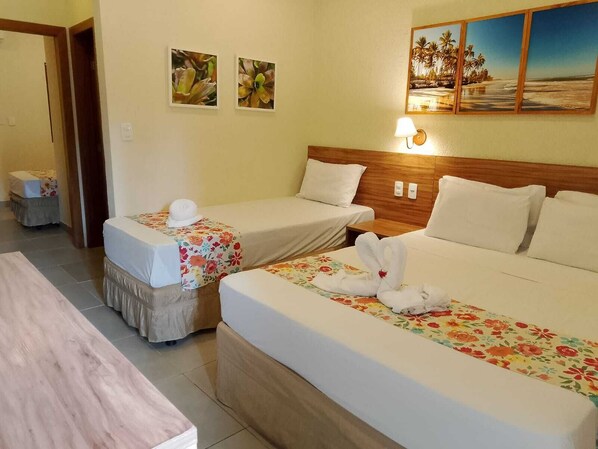 A hotel room with two single beds, a wooden headboard, a large bed with a floral bedspread, and a painting of a beach scene on the wall. - Pousada Tropicarim (Camaçari)