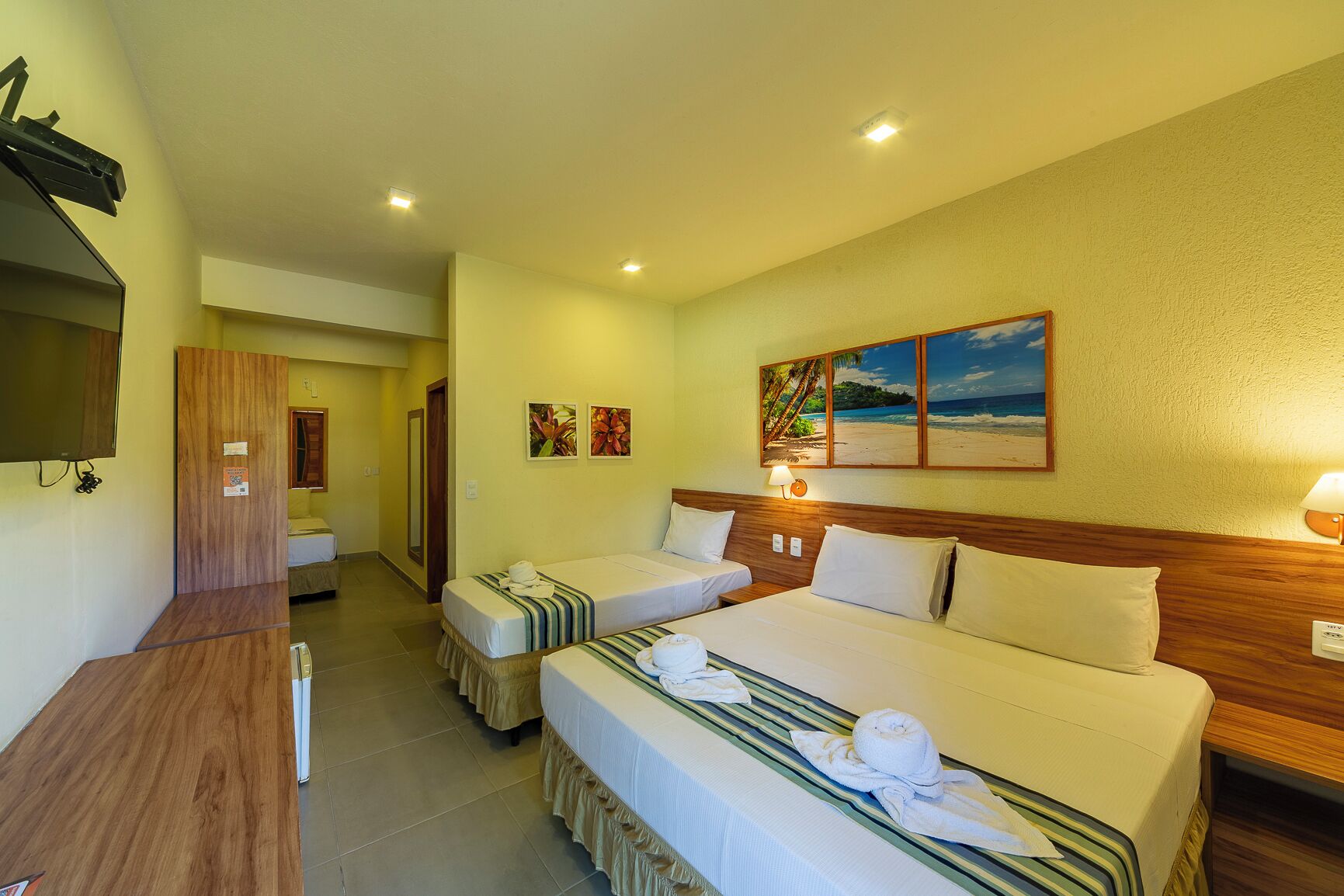 A hotel room with two beds, a TV, a painting, and a desk.