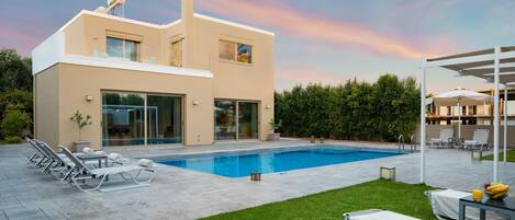 A modern two-story house with a swimming pool, outdoor seating, and a well-maintained lawn.