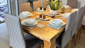 Un comedor con mesa de madera, sillas acolchadas, una planta en maceta y lámparas colgantes.