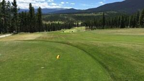 Un parcours de golf avec un ciel dégagé, des montagnes lointaines et une forêt dense.