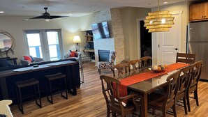Un vaste espace de vie comprenant une table à manger, des chaises en bois, un canapé et un téléviseur fixé au mur.