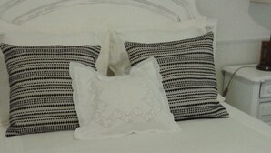 Un lit bien fait, agrémenté d’oreillers à motifs, d’un coussin décoratif et de deux petits sacs-cadeaux ornés de rubans, le tout posé sur un couvre-lit blanc.