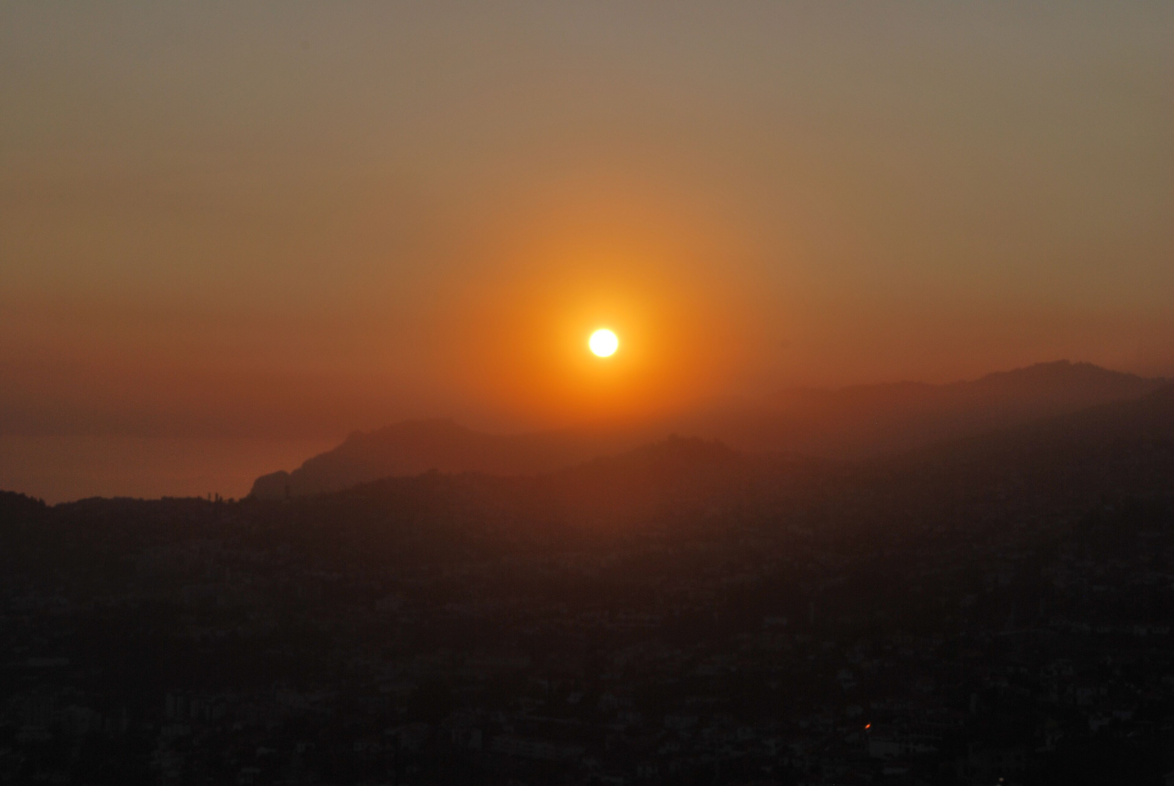 A sunset over a mountainous landscape with a silhouette of a city below.