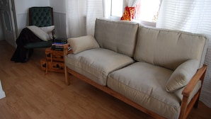 Un salon avec un canapé beige, un fauteuil vert et une table d’appoint en bois sur laquelle sont posés des livres.