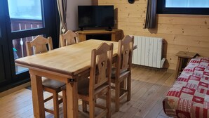 Ett mysigt rum med ett matbord i trä, stolar, en tv och en soffa.