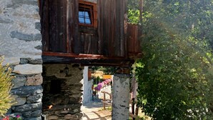 Ein rustikales Steinhaus mit einem hölzernen Balkon, Steinsäulen und einem Kopfsteinpflasterweg.