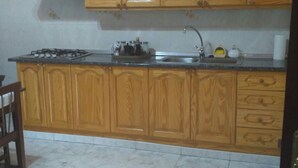 Une cuisine avec des meubles de rangement en bois, une cuisinière à gaz, un évier et un sol carrelé en marbre.