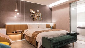 A modern hotel room with a large bed, bedside tables, a green bench, and a wall-mounted mirror.