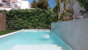 A rectangular swimming pool with clear blue water, surrounded by a low hedge and a concrete wall.