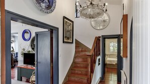 A staircase leading to a bedroom with a large window, a chandelier, and a framed picture on the wall.