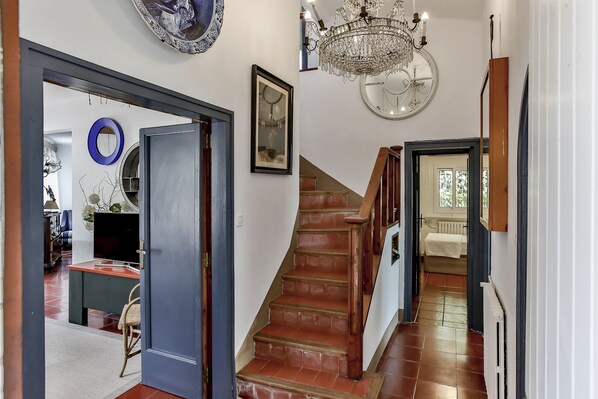 A staircase leading to a bedroom with a large window, a chandelier, and a framed picture on the wall.