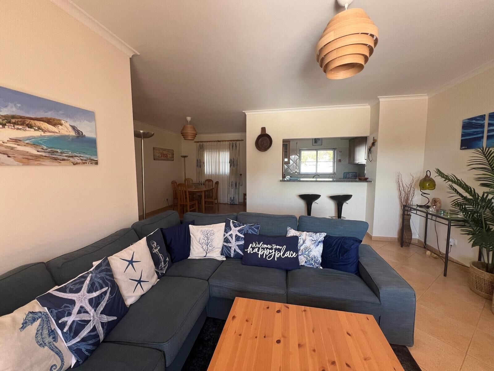 A living room with a sectional sofa, wooden coffee table, and a painting of a beach scene.