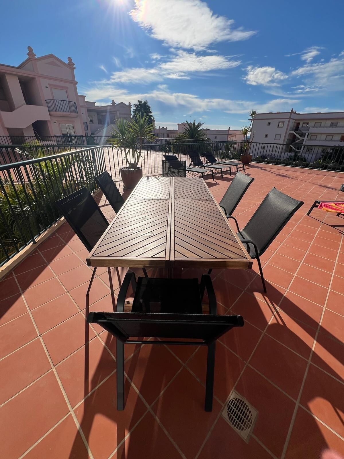 Une terrasse sur le toit, avec une longue table en bois, des chaises noires et des plantes en pot.