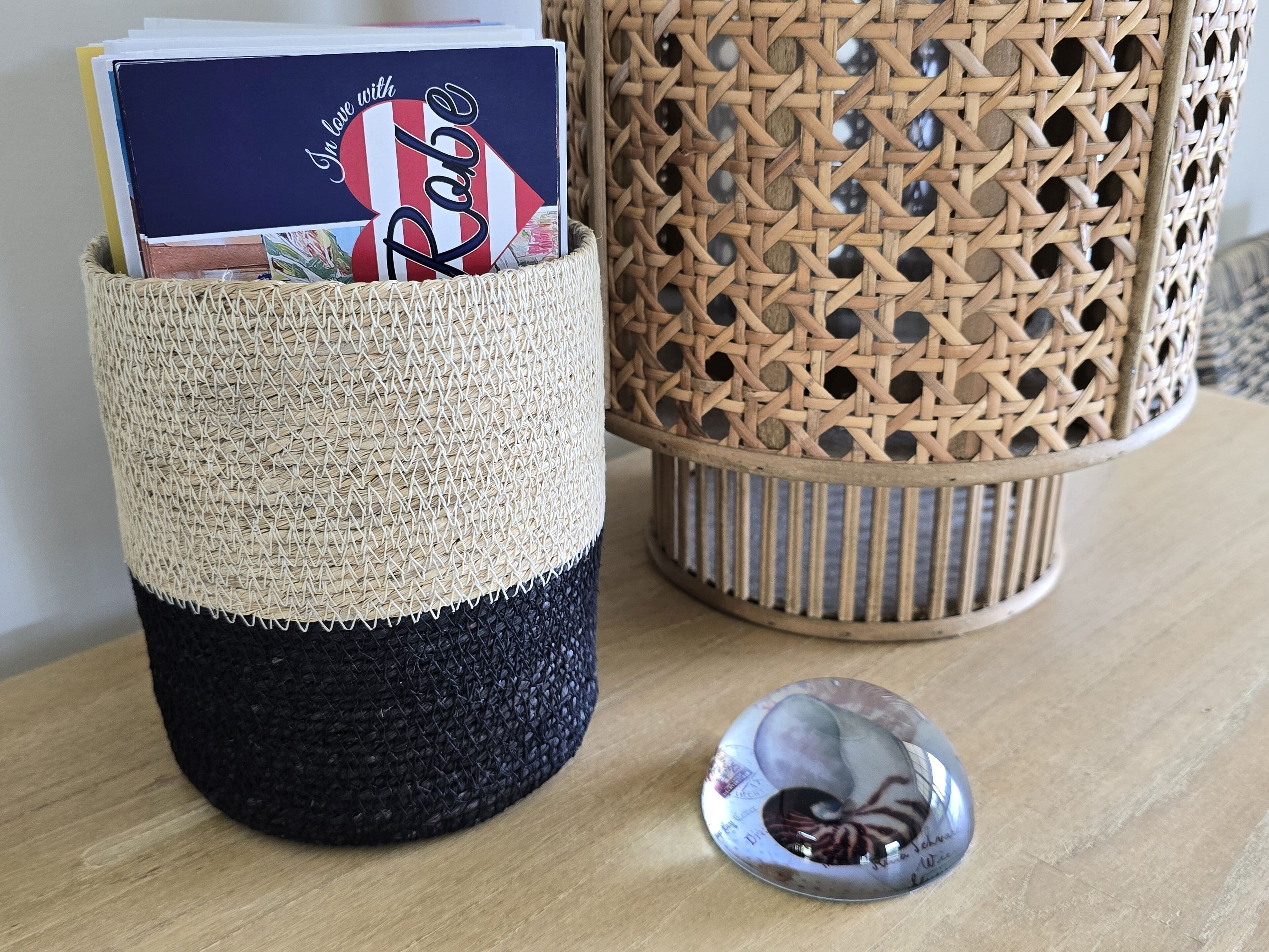 A woven basket with a book and a decorative glass object on a wooden surface.