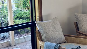 Une chaise en osier avec un coussin et un set de table tissé, sur laquelle reposent deux objets ronds, le tout placé sur une table près d’une fenêtre.