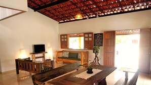 A cozy living room with a wooden dining table, benches, a sofa, and a TV. - Charming beach house with private pool, land of 8500m2 of Mata Atlantica (Ilheus)