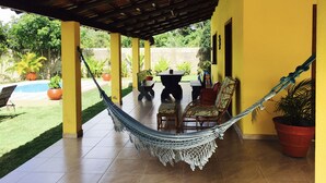 A covered patio with a hammock, outdoor furniture, and potted plants. - Charming beach house with private pool, land of 8500m2 of Mata Atlantica (Ilheus)