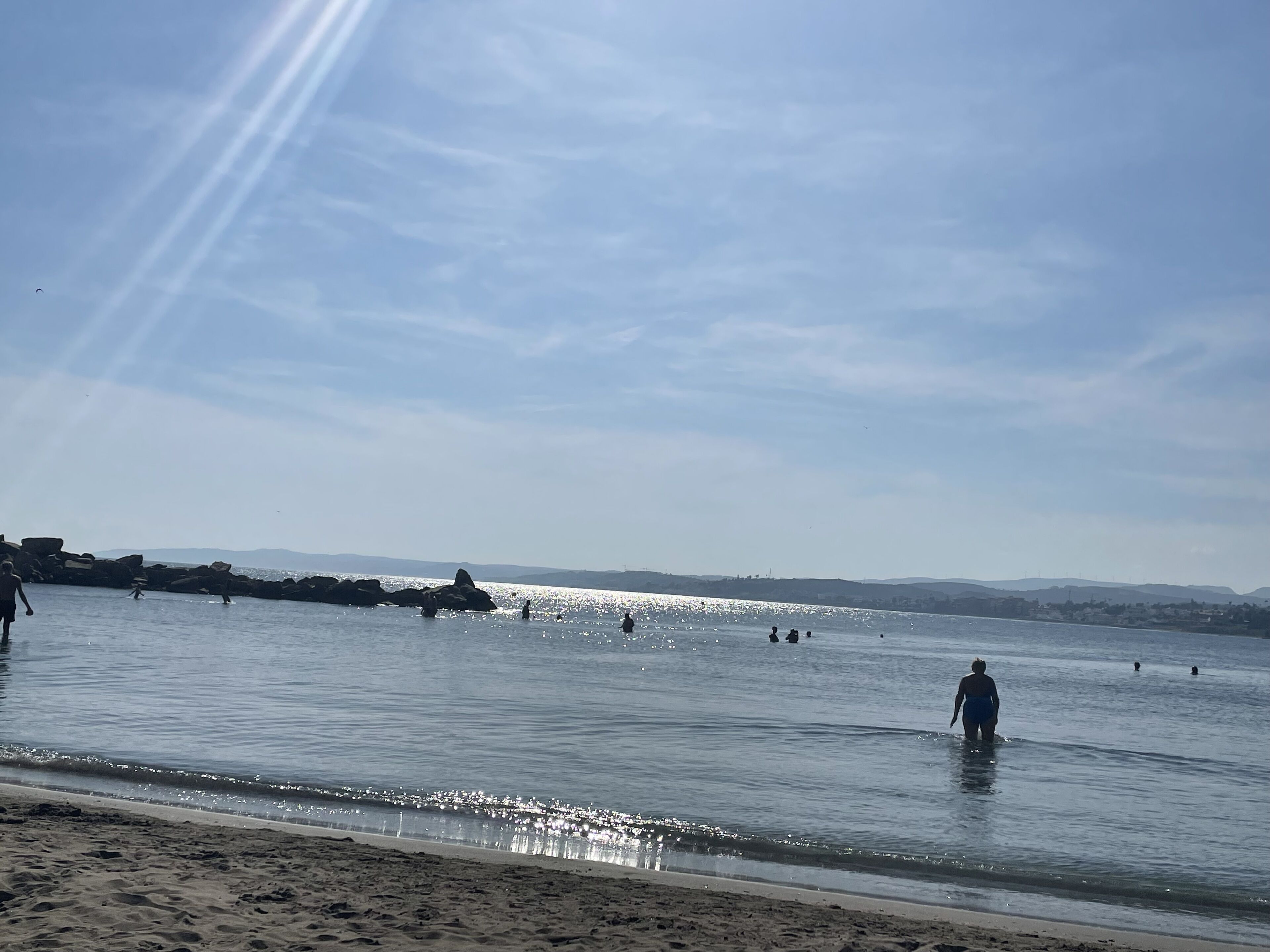 Een strand met mensen in het water en een heldere lucht.