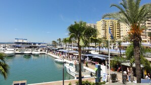 Eine Marina mit vertäuten Booten, eine Uferpromenade und ein Hotel im Hintergrund.