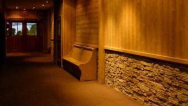 Ein Korridor mit Holzwänden und einer Wand aus Stein, der zu einer Tür am Ende führt.