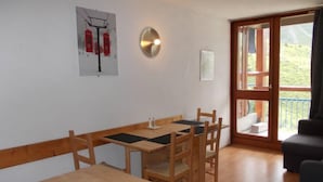Ein Essbereich mit einem Holztisch und Stühlen, einer Wandleuchte und einem Fenster mit Blick auf Grünflächen.