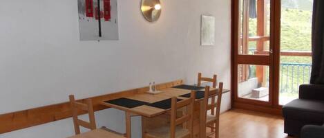 A dining area with a wooden table and chairs, a wall-mounted light, and a window with a view of greenery.