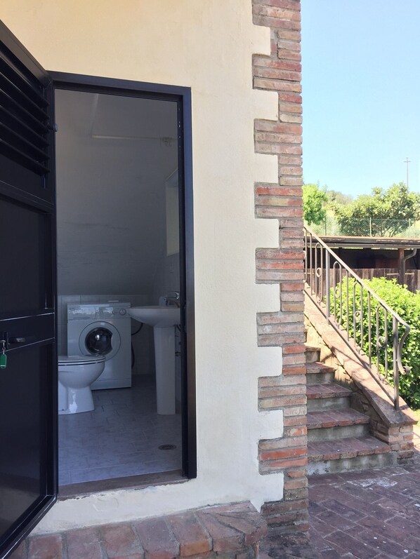 A bathroom with a washing machine and toilet, a black door, and a brick staircase leading outside.