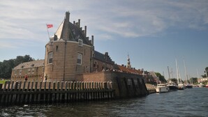 Un edificio histórico con una torre destacada, ubicado junto a una orilla con barcos amarrados.