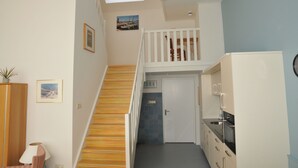 Una escalera conduce a un dormitorio tipo altillo con tragaluces, una cocina con armarios blancos y un comedor con mesa y sillas.