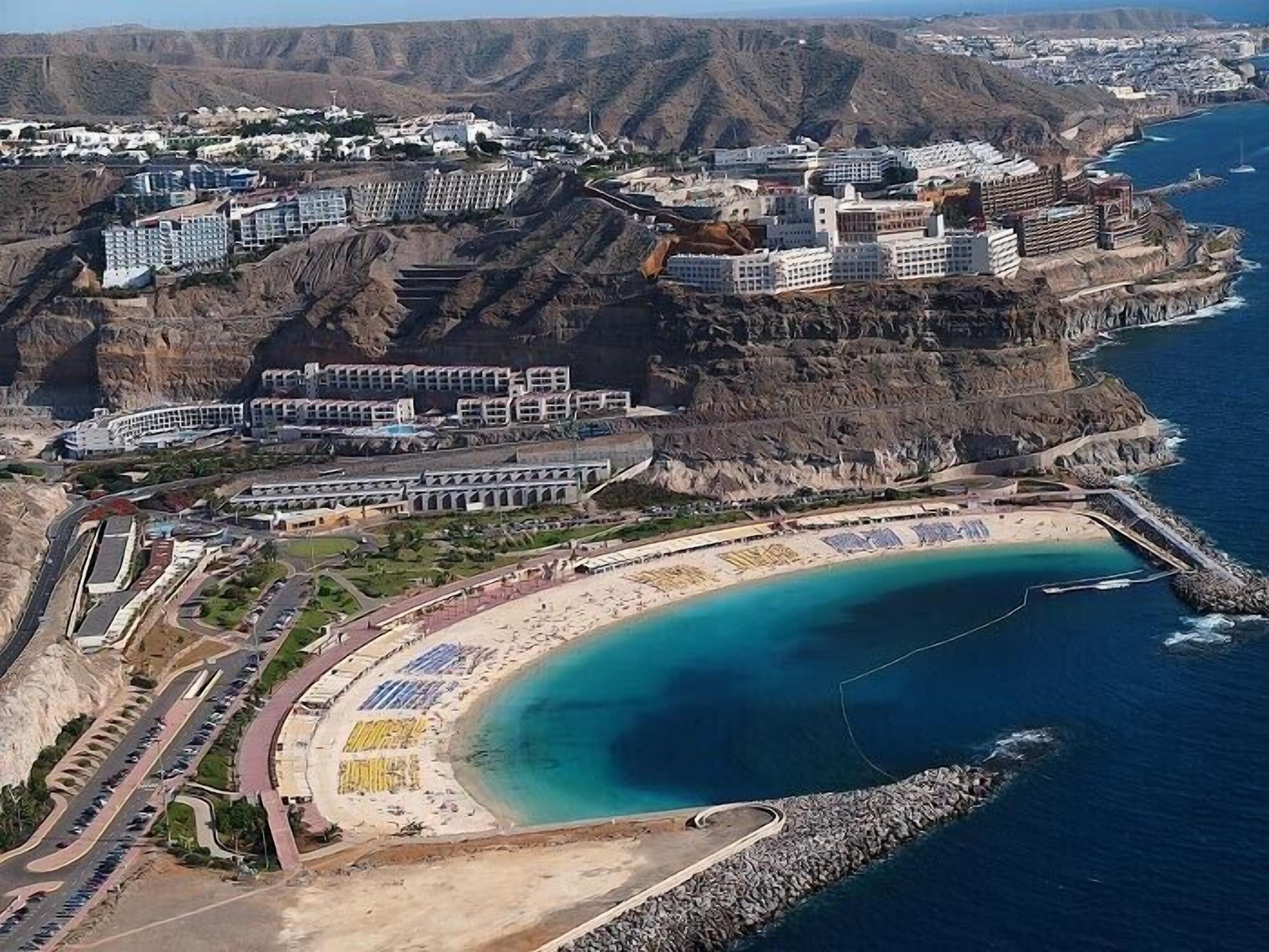 A coastal resort with multiple buildings, a beach, and a rocky cliff backdrop.