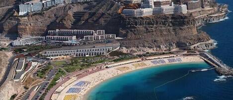 A coastal resort with multiple buildings, a beach, and a rocky cliff backdrop.