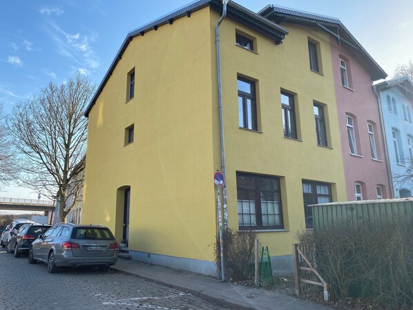 A multi-story building with a yellow facade, parked cars, and a clear sky. - Wismars old town on foot! (Wismar)