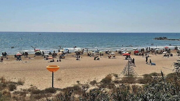 Een strand met mensen, parasols en een uitkijktoren.